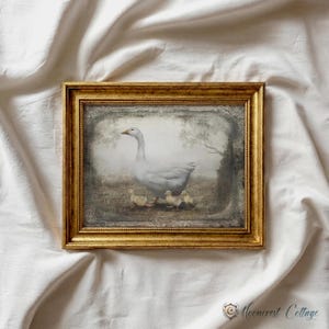 A framed painting of a mother duck and her ducklings is displayed on a white fabric background.