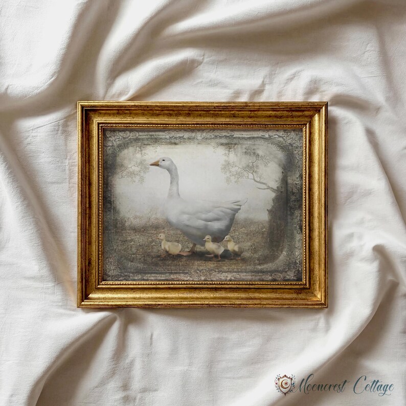 A framed painting of a mother duck and her ducklings is displayed on a white fabric background.