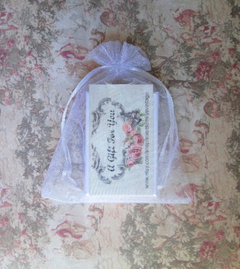 May include: A white organza gift bag tied with a ribbon, containing a card with the text "A Gift For You" and a floral design. The background features a vintage floral pattern.