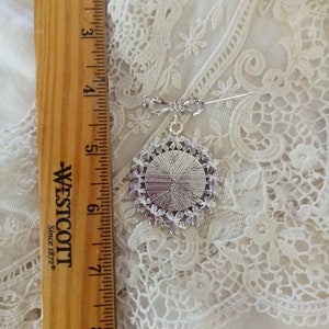 Pode incluir: Um broche de prata com um design redondo e ornamentado. O broche tem aproximadamente 5 cm de di&acirc;metro e tem um pino na parte de tr&aacute;s.