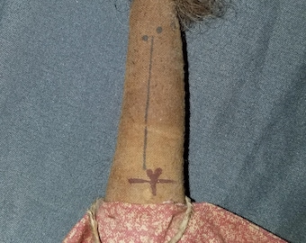 May include: A handmade rag doll with brown yarn hair, a brown fabric body, and a red and white floral print dress. The doll has a simple face with two black eyes and a brown line for a mouth. The doll is wearing a brown bell on a string around its neck.