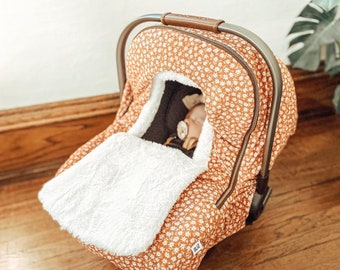 May include: A brown and white floral car seat cover with a white sherpa lining. The cover is made by the brand "Bliz".