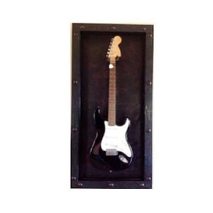 May include: A black electric guitar with a white pickguard is displayed in a dark brown wooden frame with metal accents.