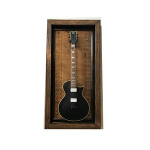 May include: A black electric guitar with a wooden frame is displayed in a dark wood frame with a brown background.