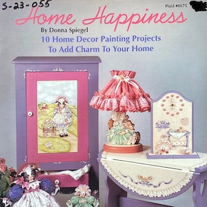 Puede incluir: Una portada de libro con el título "Home Happiness" de Donna Spiegel. La portada presenta un armario pintado de morado y rosa, una lámpara con una pantalla de color rosa con volantes, una muñeca y un reloj pintado. El libro incluye 10 proyectos de pintura de decoración del hogar para agregar encanto a tu hogar.
