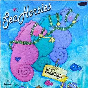 May include: A children's book cover featuring a pink, blue, and teal seahorse with a green garland. The title of the book is "Sea Horsies and Waterbugs" by Annie Lang. The cover also features two water bugs wearing goggles and building a sandcastle.