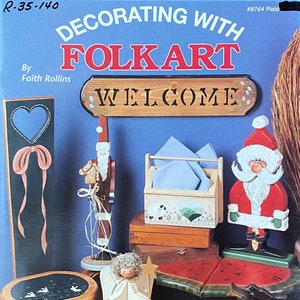 May include: A book cover with the title "Decorating with Folkart" by Faith Rollins. The cover features a variety of wooden folk art projects, including a welcome sign, a Santa Claus, an angel, and a pumpkin. The book is part of the Plaid line of craft books and is book #20 in celebration of the 20th anniversary of NSTDP.