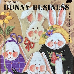 Puede incluir: Una colorida ilustración titulada "Bunny Business" con varios conejos de dibujos animados con mejillas rosadas y orejas largas. Los conejos están rodeados de flores, verduras y una sandía. La obra de arte está firmada por Susan Jill Hall.