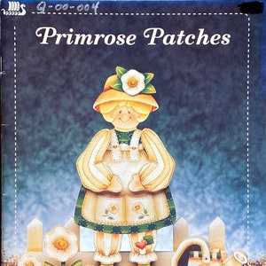 May include: A painted wooden figurine of a girl wearing a yellow hat and a green and white dress, holding a watering can. The girl is standing in front of a white picket fence with flowers. The title "Primrose Patches" and the artist's name "by Kay Quist" are printed on the image.