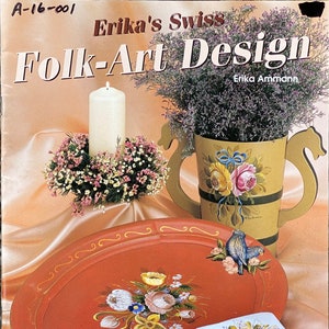 May include: A book titled "Erika's Swiss Folk-Art Design" by Erika Ammann. The cover features a painted tray with a floral design, a candle holder with a wreath of flowers, and a vase with a floral design. The book includes easy multi-load instructions.