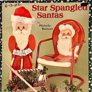 May include: A craft book titled "Star Spangled Santas" by Michelle Bastean. The cover features a painted Santa Claus on a red metal chair, a wooden Santa Claus holding a sign that says "Ho! Ho! Ho!" and a variety of Christmas-themed garden decorations.