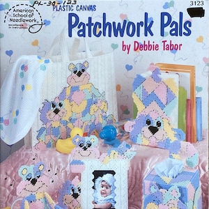May include: A set of plastic canvas craft projects featuring patchwork bear designs. The set includes a tote bag, a tissue box cover, a picture frame, and a small toy. The designs are in shades of pink, blue, yellow, and white.