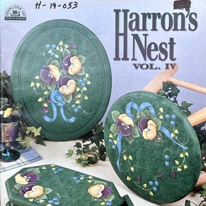 Puede incluir: Cajas y tapas decorativas verdes con diseños florales pintados a mano. Las tapas son ovaladas y la caja es un octágono verde oscuro con un cajón. El diseño floral incluye acentos morados, amarillos y azules. El texto "Harron's Nest Vol. IV" es visible.