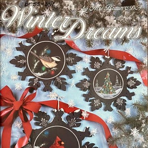 Puede incluir: Adornos decorativos de copos de nieve con escenas invernales. Cada copo de nieve negro presenta una imagen circular de un pájaro, un árbol de Navidad y un cardenal rojo. Cinta roja y nieve artificial completan el tema invernal. El texto "Winter Dreams" es visible.