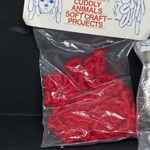 May include: A package of red curly chenille yarn, labeled "Curly Chenille" and "Blue Jay Brand". The package says "Use for Doll's Hair, Cuddly Animals, Soft Craft Projects".