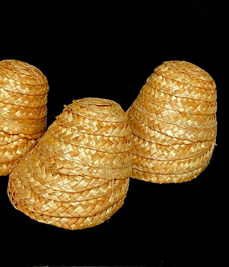 Pu&ograve; includere: Tre cappelli di paglia intrecciata di forma conica sono esposti su sfondo nero. I cappelli sono di colore giallo dorato e sembrano essere fatti di paglia fittamente intrecciata. I cappelli sono impilati e hanno una parte superiore arrotondata.