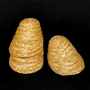 Pu&ograve; includere: Due piccoli cappelli di paglia intrecciata a forma conica. I cappelli sono fatti di paglia marrone chiaro, fittamente intrecciata, e hanno un bordo leggermente svasato. Un cappello &egrave; impilato sopra altri, mentre l'altro &egrave; separato.