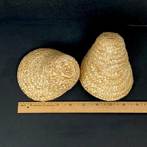 May include: Two woven straw items, one round and one cone-shaped, sit on a black surface. The round item is approximately 4 inches in diameter. A wooden ruler with inch markings is placed near the items.