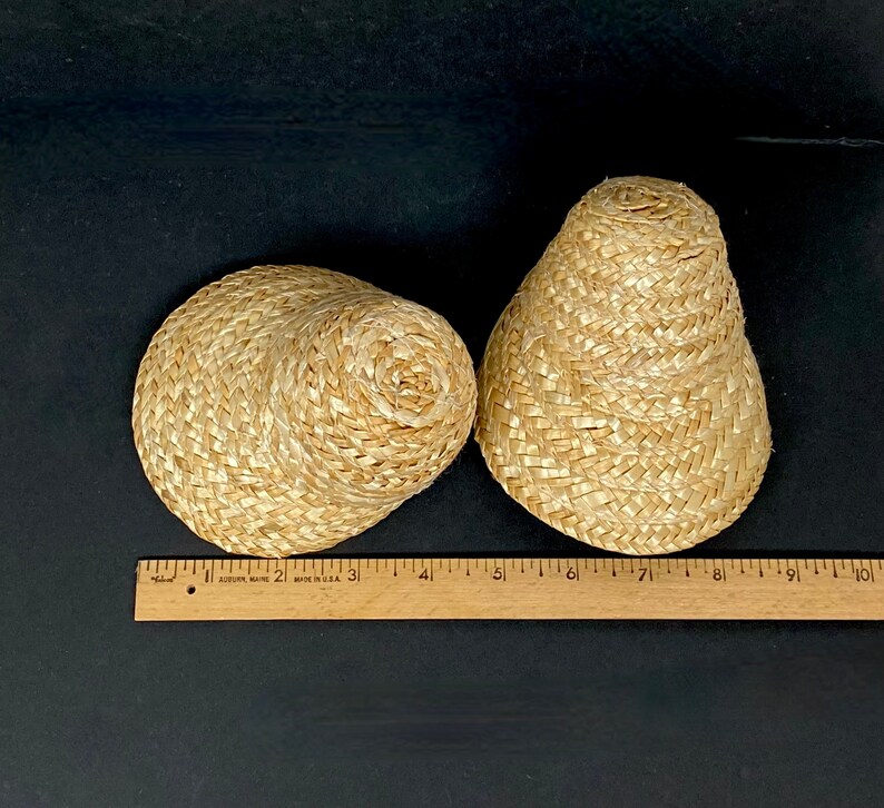 May include: Two woven straw items, one round and one cone-shaped, sit on a black surface. The round item is approximately 4 inches in diameter. A wooden ruler with inch markings is placed near the items.