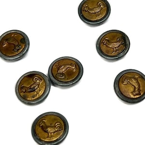 Puede incluir: Ocho botones de tono plateado y dorado con un diseño de gallo. Los botones son redondos y tienen un diseño en relieve de un gallo.