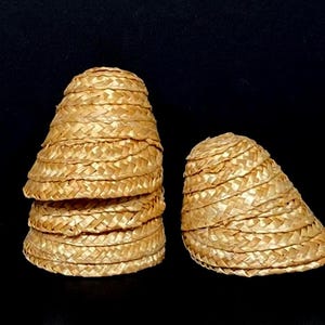 Pu&ograve; includere: Diversi piccoli cappelli di paglia intrecciata sono esposti su uno sfondo nero. I cappelli sono a forma di cono, con un'ampia tesa e un motivo a trama fitta. I cappelli sono di colore marrone chiaro.