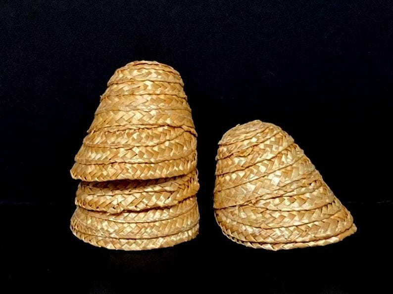Pu&ograve; includere: Diversi piccoli cappelli di paglia intrecciata sono esposti su uno sfondo nero. I cappelli sono a forma di cono, con un'ampia tesa e un motivo a trama fitta. I cappelli sono di colore marrone chiaro.