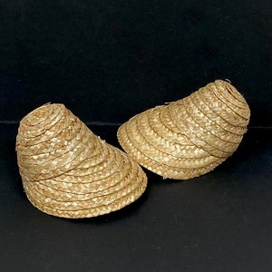 May include: Two straw sun visors. The visors are made of woven straw and have a curved brim. The visors are a light tan color and are sitting on a black surface.