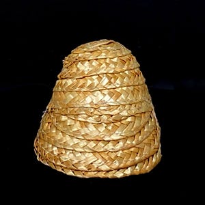 Pu&ograve; includere: Un cappello di paglia intrecciata a forma conica. Il cappello &egrave; realizzato in paglia marrone chiaro, fittamente intrecciata, con una serie di fasce orizzontali che ne creano la forma. La trama del cappello &egrave; visibile, su sfondo nero.