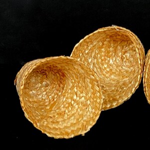 Pu&ograve; includere: Tre piccoli cappelli di paglia intrecciata di colore marrone chiaro naturale. I cappelli sono rotondi con una forma leggermente conica e il motivo dell'intreccio &egrave; visibile. Lo sfondo &egrave; nero.