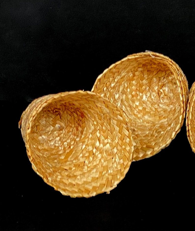 Pu&ograve; includere: Tre piccoli cappelli di paglia intrecciata di colore marrone chiaro naturale. I cappelli sono rotondi con una forma leggermente conica e il motivo dell'intreccio &egrave; visibile. Lo sfondo &egrave; nero.