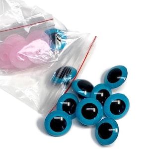 May include: A bag of turquoise blue plastic safety eyes with black pupils. The eyes are in a clear plastic bag with a red zipper.