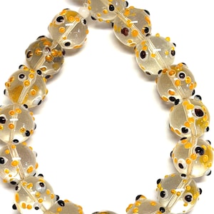 May include: A strand of clear glass beads with yellow and black dot patterns. The beads are round and have a slightly irregular shape. The beads are strung on a clear string, and the background is white.
