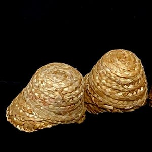 Pu&ograve; includere: Diversi piccoli cappelli di paglia intrecciata, di colore marrone dorato naturale, sono disposti su uno sfondo nero. I cappelli hanno una corona arrotondata e un bordo leggermente svasato, che mostra un motivo a trama fitta. I cappelli sembrano fatti a mano.