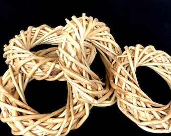 May include: Three woven wreath-shaped objects made of light brown, natural-looking twigs. The wreaths are intertwined, with a dark background. The twigs are tightly woven together, creating a textured surface.