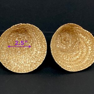 May include: Two woven, bowl-shaped baskets made of natural-colored straw. Each basket is approximately 2.5 inches in diameter. The baskets are displayed on a dark surface.