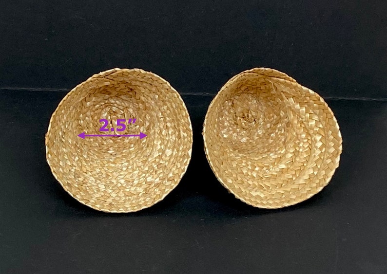 May include: Two woven, bowl-shaped baskets made of natural-colored straw. Each basket is approximately 2.5 inches in diameter. The baskets are displayed on a dark surface.