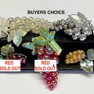 Puede incluir: Una colección de uvas de vidrio iridiscente con hojas. Las uvas son de varios colores, incluyendo transparente, plata, oro y rojo. El texto "BUYERS CHOICE" está en la parte superior de la imagen. El texto "RED SOLD OUT" está debajo de dos de los racimos de uvas.