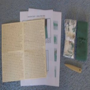 以下が含まれることがあります： 印刷された説明書、布地、小さなツールなど、さまざまな縫製用品。 説明書はクリーム色の紙に印刷されており、布地には花柄と無地の緑色の部分が含まれています。 小さな黄色のツールも含まれています。