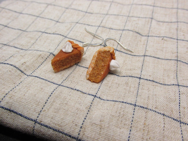 K&ouml;nnte beinhalten: Ein Paar H&auml;ngeohrringe mit Miniatur-K&uuml;rbiskuchenst&uuml;cken mit wei&szlig;em Frosting. Die Ohrringe sind aus Polymer Clay gefertigt und haben silberne Haken.