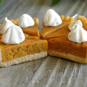 K&ouml;nnte beinhalten: Nahaufnahme einer Mini-K&uuml;rbis-Tarte mit einer flockigen Kruste und einem Klecks wei&szlig;er Baiser auf der Oberseite. Die Tarte liegt auf einer Holzoberfl&auml;che.