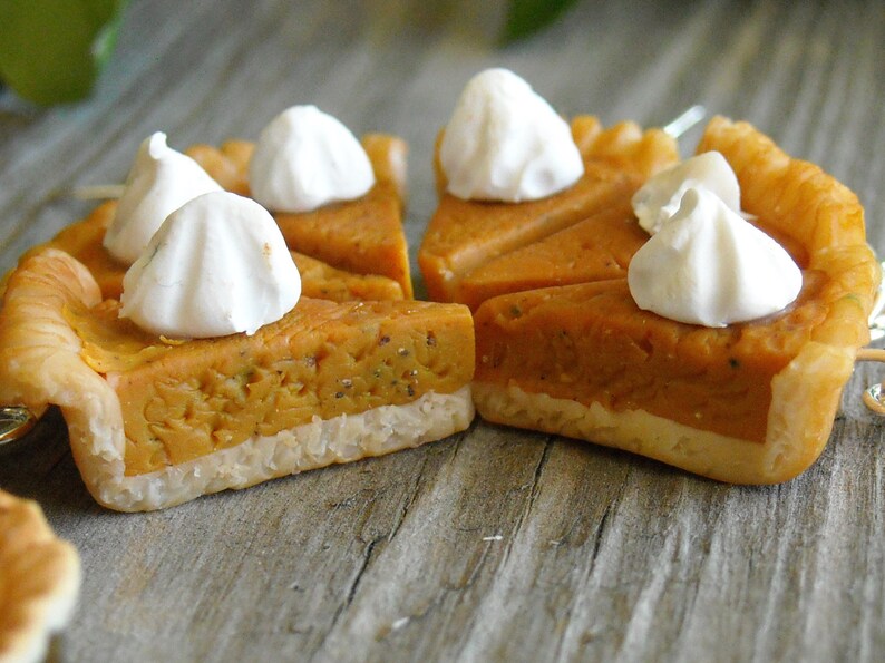 K&ouml;nnte beinhalten: Nahaufnahme einer Mini-K&uuml;rbis-Tarte mit einer flockigen Kruste und einem Klecks wei&szlig;er Baiser auf der Oberseite. Die Tarte liegt auf einer Holzoberfl&auml;che.