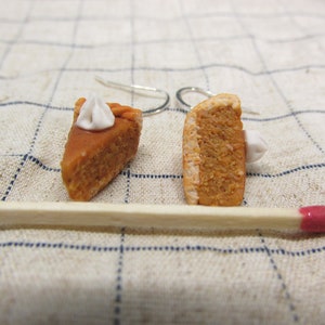 K&ouml;nnte beinhalten: Ein Paar H&auml;ngeohrringe mit Miniatur-K&uuml;rbiskuchenst&uuml;cken mit wei&szlig;em Frosting. Die Ohrringe sind aus Polymer Clay gefertigt und haben silberne Haken.