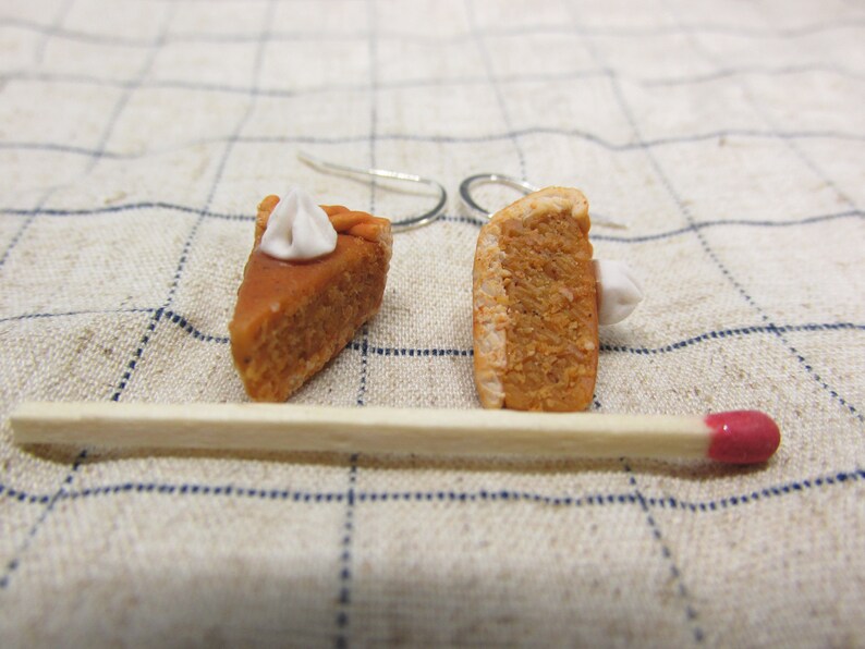 K&ouml;nnte beinhalten: Ein Paar H&auml;ngeohrringe mit Miniatur-K&uuml;rbiskuchenst&uuml;cken mit wei&szlig;em Frosting. Die Ohrringe sind aus Polymer Clay gefertigt und haben silberne Haken.