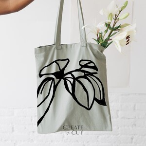 Op de afbeelding: Een lichtgroene tote bag met een zwarte lijntekening van een plant op de voorkant. De tas heeft de tekst "CREATE THE CUT" onderaan gedrukt.