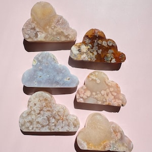 May include: Six cloud-shaped decorative stones in various colors, including beige, brown, and light blue. The stones have a textured appearance and are arranged on a pink surface. These stones are ideal for home decor or as unique gifts.