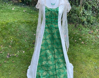 Puede incluir: Un vestido de novia blanco y verde con una cola larga y un velo de encaje. El vestido tiene un corpiño verde con un patrón dorado y una falda blanca.