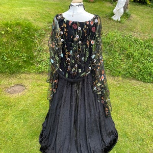 May include: A black velvet gown with a sheer overlay featuring floral embroidery in shades of orange, green, and white. The gown has a fitted bodice and a flowing skirt.