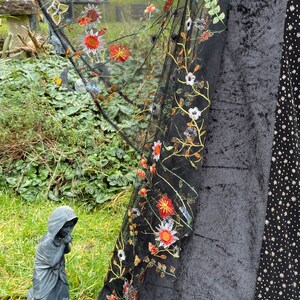 May include: Black sheer fabric with embroidered flowers and a butterfly design. The fabric is draped over a black velvet surface.