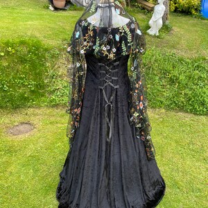 May include: A black velvet gown with a lace overlay featuring floral embroidery. The gown has a fitted bodice with a lace-up back and a flowing skirt.