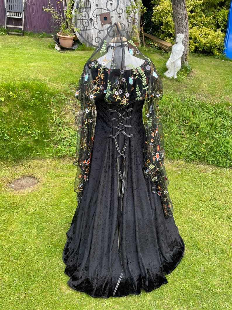May include: A black velvet gown with a lace overlay featuring floral embroidery. The gown has a fitted bodice with a lace-up back and a flowing skirt.